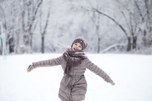 Little girl running on the background of snow covered winter park