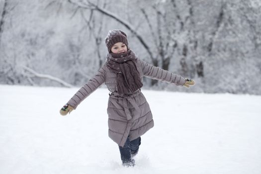 Little girl running on the background of snow covered winter park