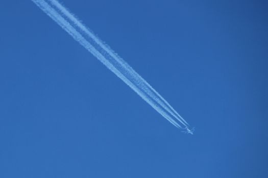 Aeroplane flying through clear blue sky with vapour trails