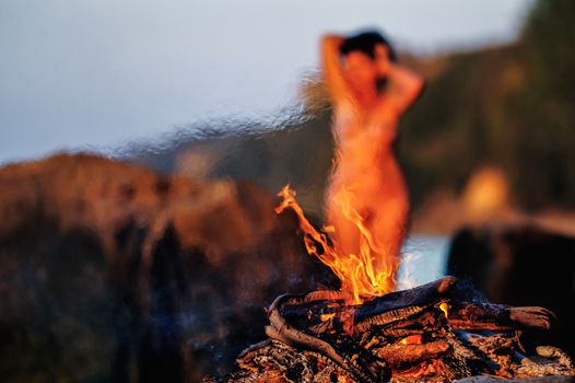Nude woman on beach near the campfire