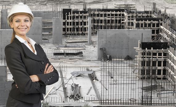 Beautiful businesswoman in suit and helmet standing with crossed arms. Construction site in background. Building concept