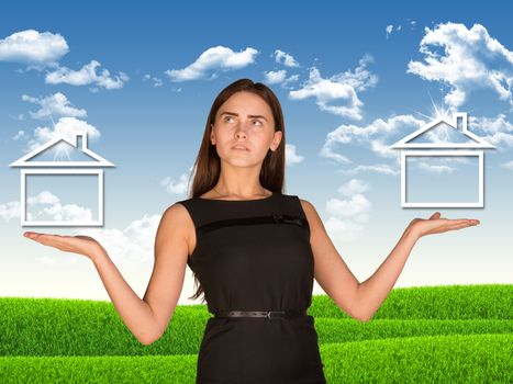 Businesswoman holding two houses as if chosing. Green lawn and sky with clowds as backdrop