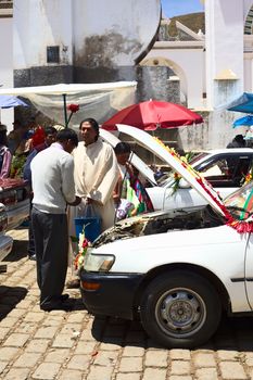 COPACABANA, BOLIVIA - OCTOBER 20, 2014: Unidentified priest blesses driver/owner of a car at the blessing of automobiles in front of the basilica on 6 de Agosto avenue in the center of the small tourist town on October 20, 2014 in Copacabana, Bolivia. Almost every day many cars, taxis, buses and vans are standing in line to receive blessing from a priest of the basilica.