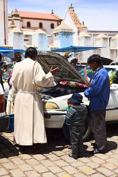 COPACABANA, BOLIVIA - OCTOBER 20, 2014: Priest saying a prayer in front of the open hood of a car at the blessing of vehicles on 6 de Agosto avenue outside the basilica in the small tourist town on October 20, 2014 in Copacabana, Bolivia. 