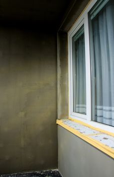 Semifinished repairing of balcony, gray plaster and dirty white window.