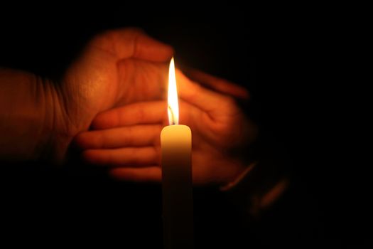 hand protects the flame from a candle burning on a dark background