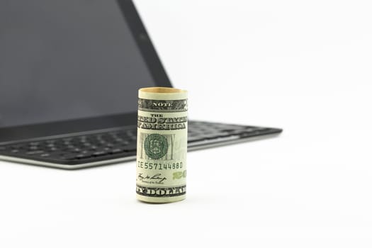 Focus on American dollar standing upright in front of tablet and keyboard.  Selective focus on money with copy space to right. 