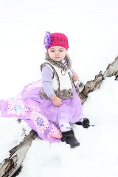 Little girl sitting on a log in the snow