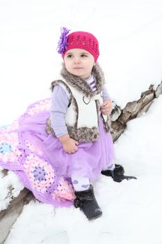 Little girl sitting on a log in the snow