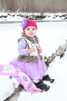Little girl sitting by a snowy river
