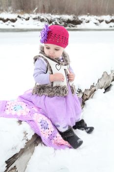 Little girl sitting on a log in the snow