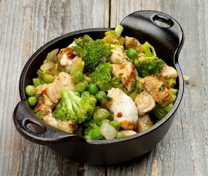 Delicious Homemade Chicken Stew with Green Pea, Broccoli and Bell Pepper in Black Saucepan isolated on Rustic Wooden background