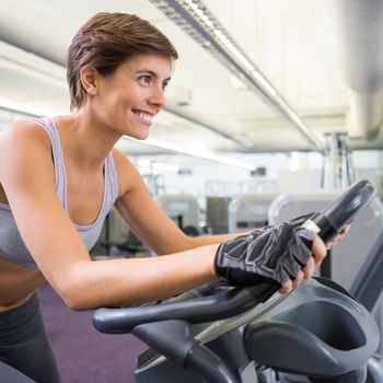 Fit smiling woman working out on the exercise bike at the gym