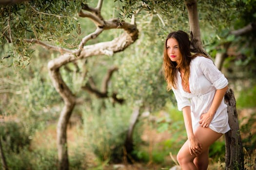 Attractive, young brunette on the beach, amid olive trees, looking both sensual and natural
