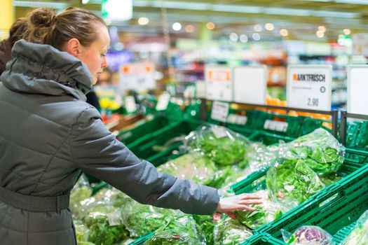 Beautiful, young woman shopping for fruits and vegetables in produce department of a grocery store/supermarket (shallow DOF; color toned image)