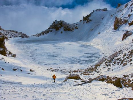 Hiker in crater with frozen lake on Sabalan, volcano in north Iran