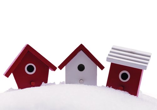 Three small red and white wooden bird houses in the snow
