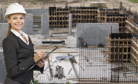 Beautiful businesswoman in suit and helmet holding paper holder and writing. Construction site in background. Building concept