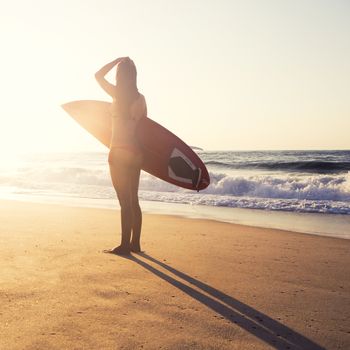 Beautiful young girl in the beach with her surfboard