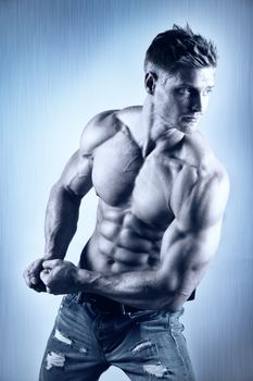 Posing young well trained man with perfect abdominal and pectoral muscle on blue metal background