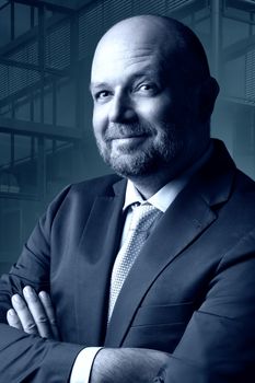 Thoughtful businessman in dark suit and tie in front of blue background