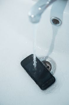 Smartphone in sink with flowing water. Vertical photo