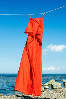 Red sundress hanging on a rope on the seashore