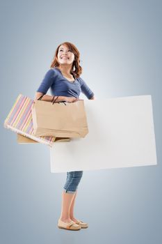 Shopping woman holding bags and blank board, full length portrait isolated.