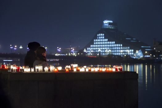RIGA, LATVIA - NOVEMBER 11: Unidentified couple at commemoration of Soldiers Memorial Day. People light candles to commemorate victory over Russian German militia it was keypoint in birth of Latvia as independent nation. New Building of National Library in background.