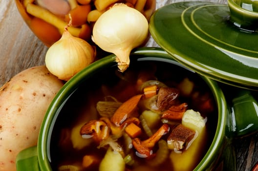 Homemade Delicious Vegetarian Soup with Chanterelle Mushrooms in Green Pot with Lid and Raw Ingredients closeup on Wooden background