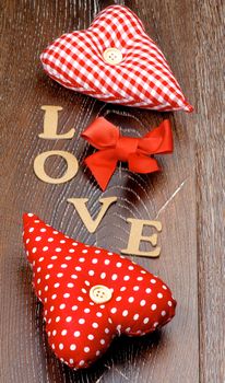 Arrangement of Two Handmade Textile Red Polka Dot Hearts, and Cardboard Word Love and Red Bow closeup on Dark Wooden background