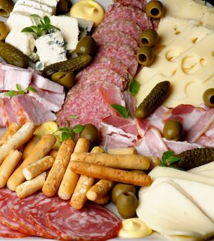 Background of Various Delicious Cheeses, Smoked Meat and Smoked Salami with Gherkins,Green Olives and Bread Sticks closeup