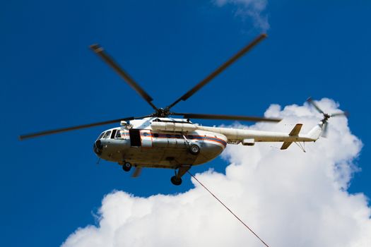 Firefighting helicopter with fire bucket flies against a clear blue sky