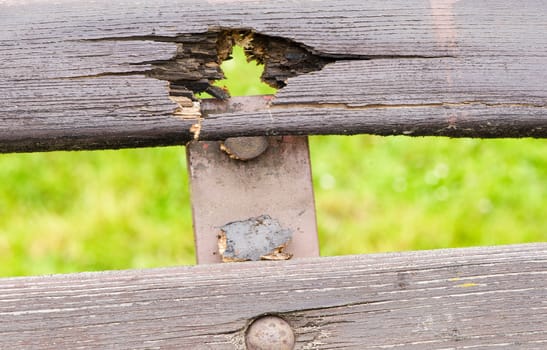 Old damaged wooden brown paint bench on green grass blur background.