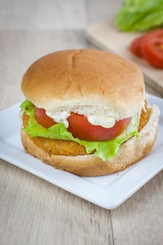 A chicken sandwich with fresh tomato and lettuce on a white plate.