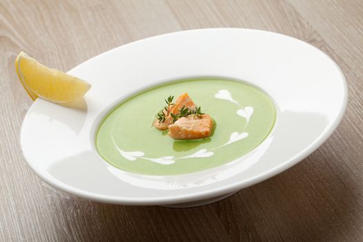 Green cabbage broccoli cream soup puree in white plate  served with  filleted salmon pieces , lemon and  theme