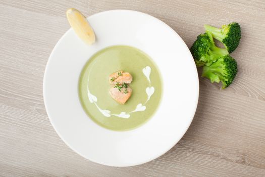 Green cabbage broccoli cream soup puree in white plate  served with  filleted salmon pieces , lemon and  theme