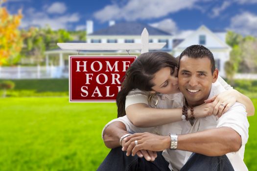 Young Happy Hispanic Young Couple in Front of Their New Home and For Sale Real Estate Sign.