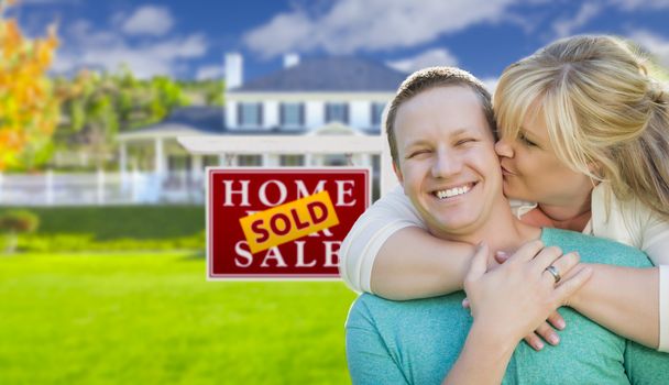 Happy Couple Hug In Front of Sold Real Estate Sign and Beautiful New House