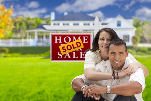 Young Happy Hispanic Young Couple in Front of Their New Home and Sold For Sale Real Estate Sign.