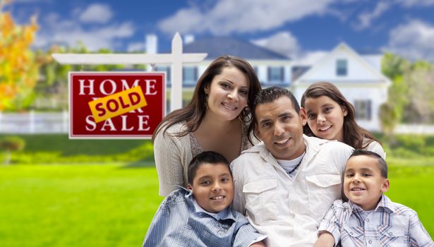 Happy Hispanic Family in Front of Their New House and Sold Home For Sale Real Estate Sign.
