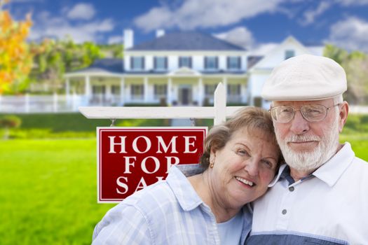 Happy Senior Couple Front of For Sale Real Estate Sign and House.