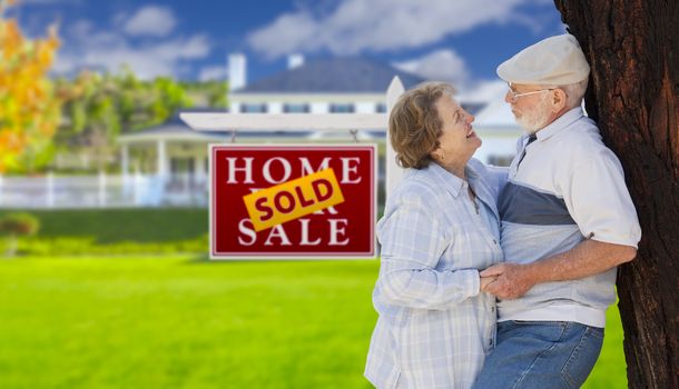 Sold Real Estate Sign with Happy Affectionate Senior Couple Hugging in Front of House.