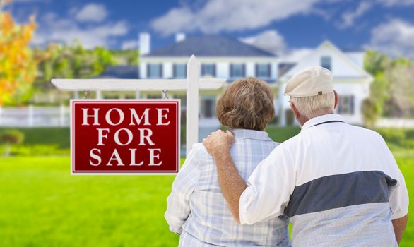 Happy Senior Couple Front of For Sale Real Estate Sign and House.