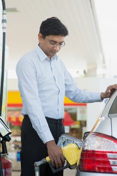 Pumping gas. Asian Indian man pumping gasoline fuel in car at gas station.