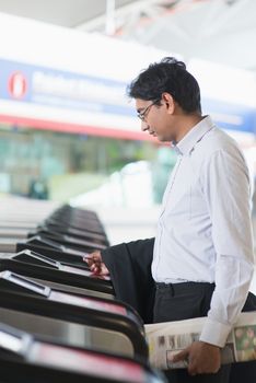 Asian Indian businessman at entrance of railway station, touching ticket token on gate barrier.