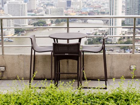 Rattan oone table with two stool chairs standing against the terrace