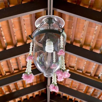 Thai style a glass lamp shade with flower garland decoration hanging in home.