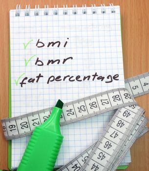 Measuring tape, a marker and a notepad with a words bmi, bmr and fat percentage