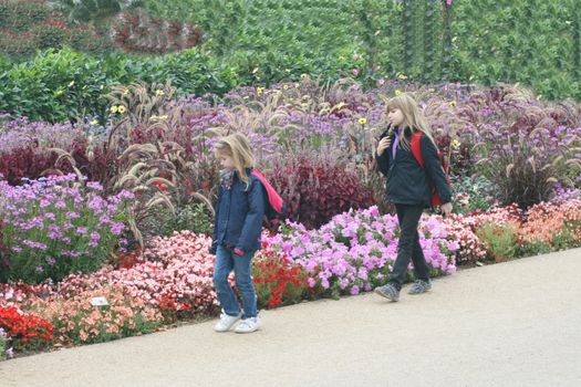 two blonde girls and colorful flower beds